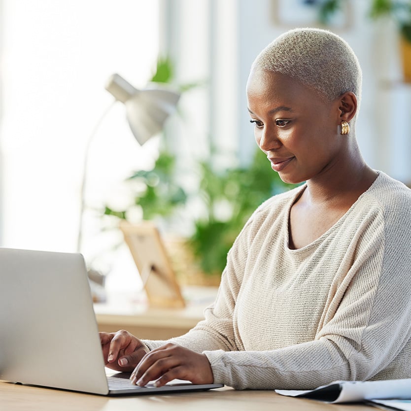 A woman focused and working on a laptop in a home office setting.