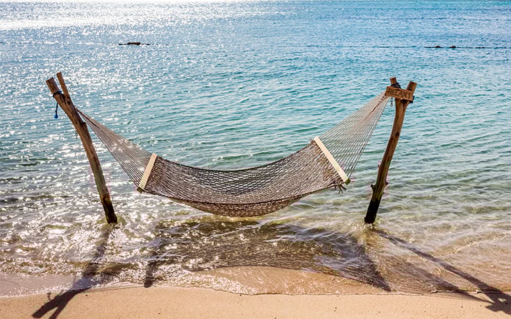 A hammock tied between two wooden posts protruding from the sandy beach.